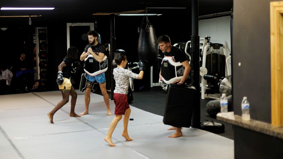 Coach Elijah Halloun holding a body shield for a youth kickboxing student