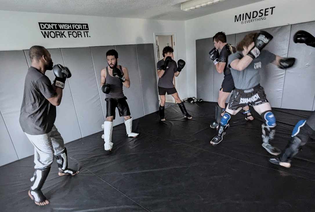 Partners in gloves and shin guards working kickboxing drills under a wall sign that reads Don't wish for it. Work for it.