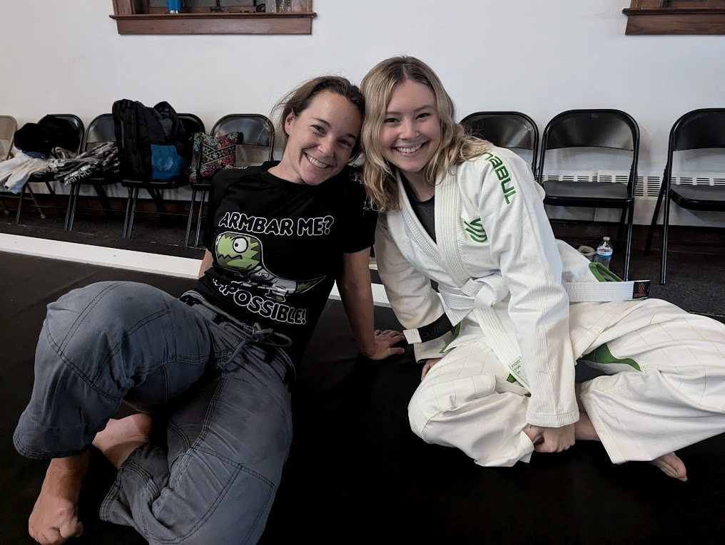 Two members smiling on the jiu jitsu mat after class